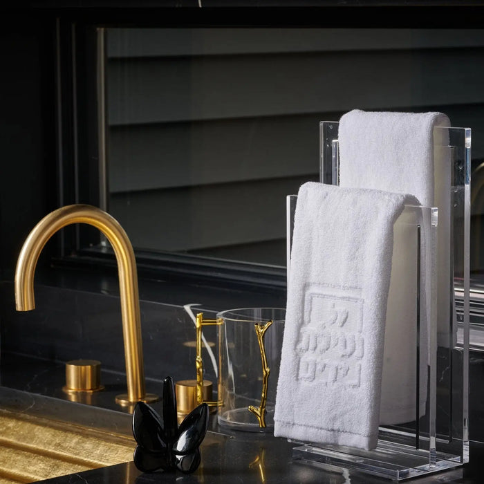 White embossed Netilas Yadayim finger towel displayed next to gold faucet and bathroom accessories on vanity shelf.
