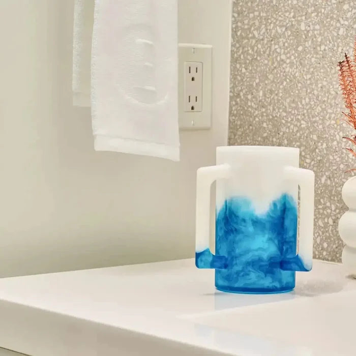 Ombre resin washing cup in blue gradient displayed on white bathroom counter next to towel