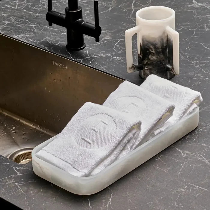 Ombre resin washing cup in cream and charcoal displayed on marble vanity with black faucet and candle holder nearby.