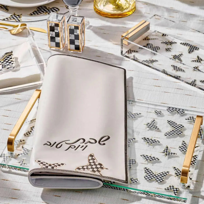 Onyx Butterfly Challah Cover in silver and gold leather displayed on a patterned tablecloth with matching table settings and decorative elements.