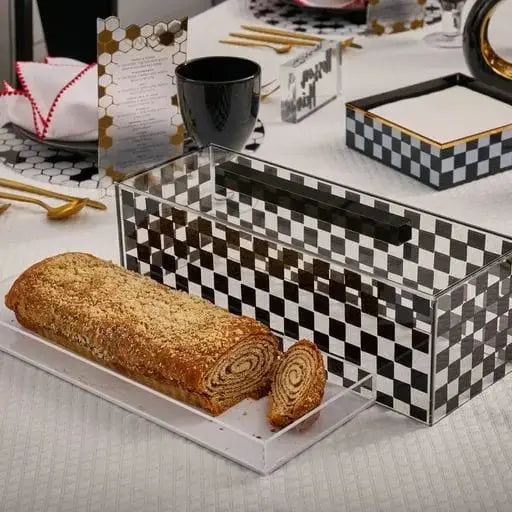 Onyx checkered cake dome with clear acrylic cover displayed with fresh bread on white surface, black and white geometric pattern serveware.