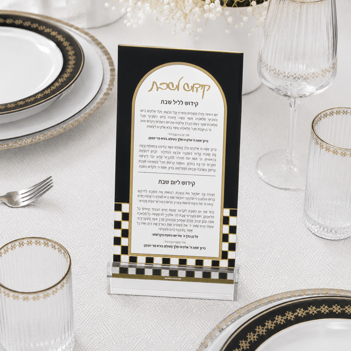 A clear acrylic ONYX KIDDUSH CARDwith a black and gold design, displayed on a white tablecloth surrounded by plates, glasses, and a fork.