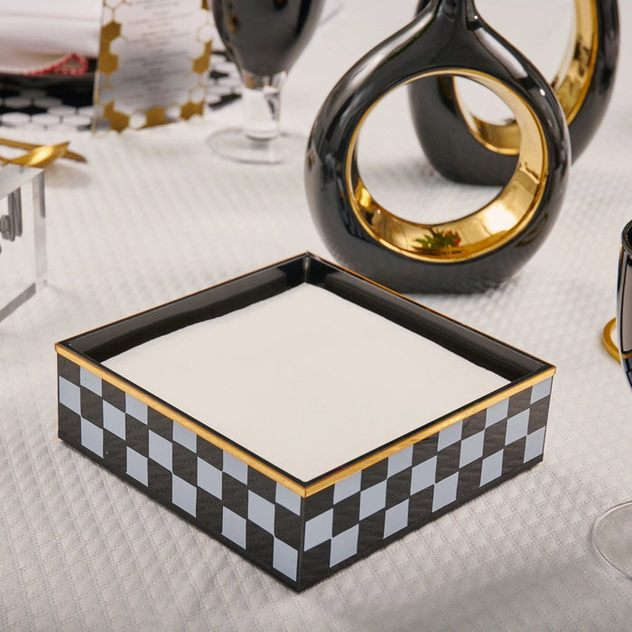 Onyx Napkin Holder with black and white checkered pattern and gold-tone trim, displayed on white surface with tabletop decor