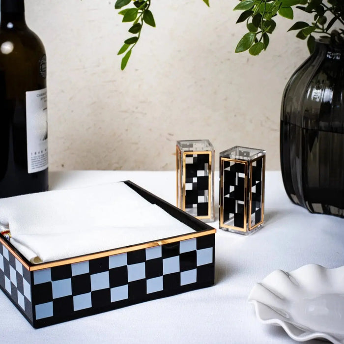Onyx napkin holder with black and white checkered pattern displayed on white surface alongside decorative bottles and plants