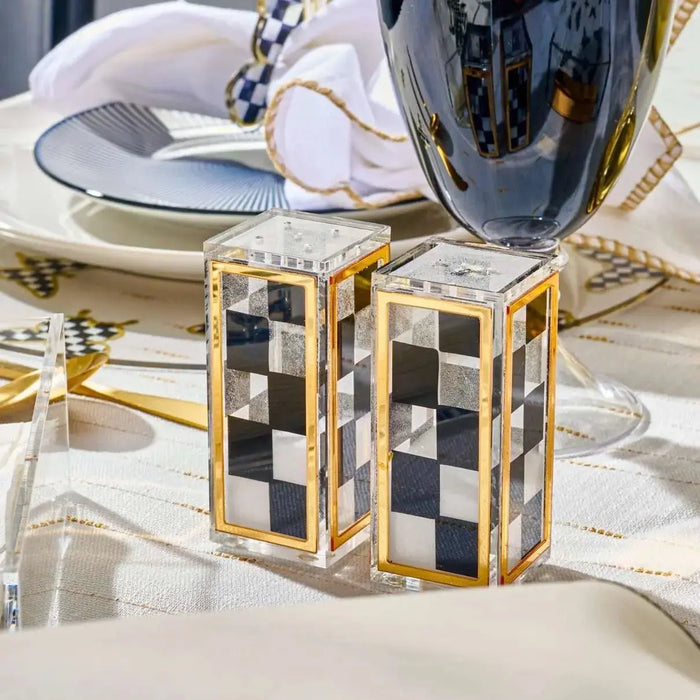 Pair of black onyx salt shakers with gold-tone metal accents and checkered design details, displayed on white tabletop setting.
