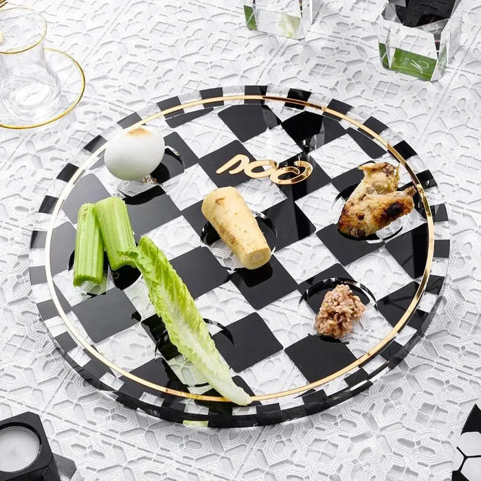 Black and white checkered Onyx Seder Plate with compartments filled with traditional Passover foods and ceremonial items arranged on a patterned tablecloth.