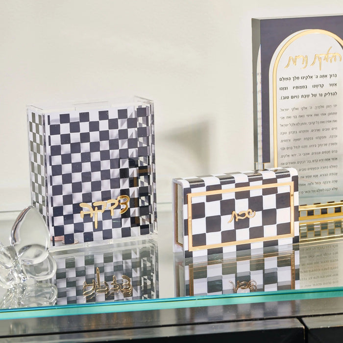 Onyx Waterdale Tzedakah Box with checkered pattern displayed on glass shelf alongside matching smaller box and candles.