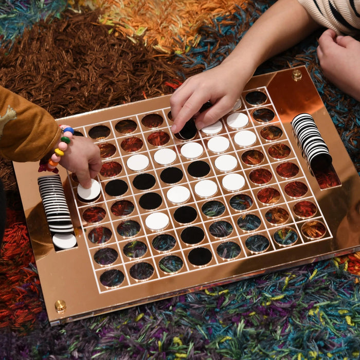 Wooden Othello game board with black and white disc pieces arranged on squares, displayed on a colorful patterned surface.