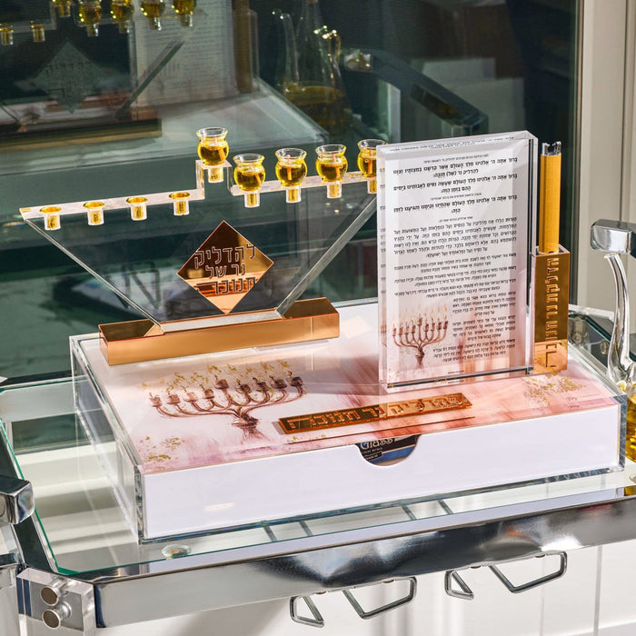 Chanukah candle lighting set on a glass shelf with a clear Lucite menorah, gold cups, a printed brachos card and the painted menorah tray with drawer