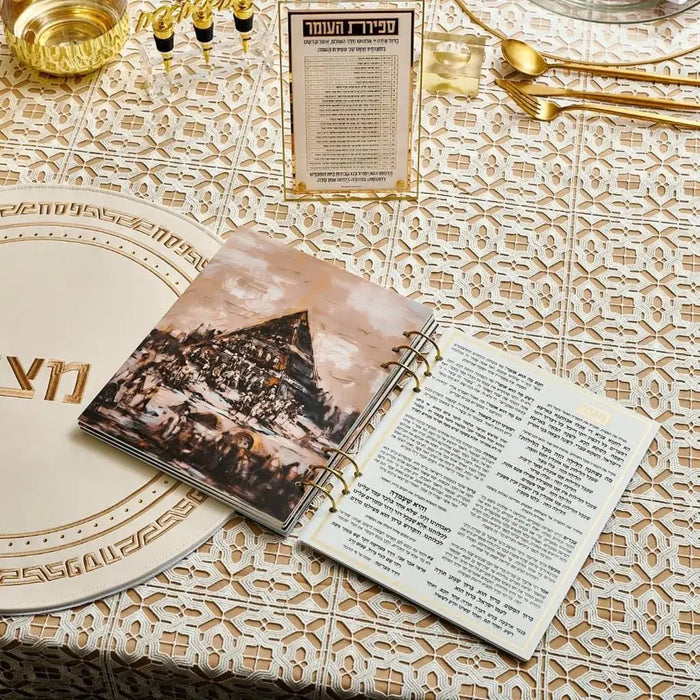 Painted by Batya Lucite Haggadah with open pages displayed on beige patterned tablecloth alongside gold Pesach dinnerware and traditional items.
