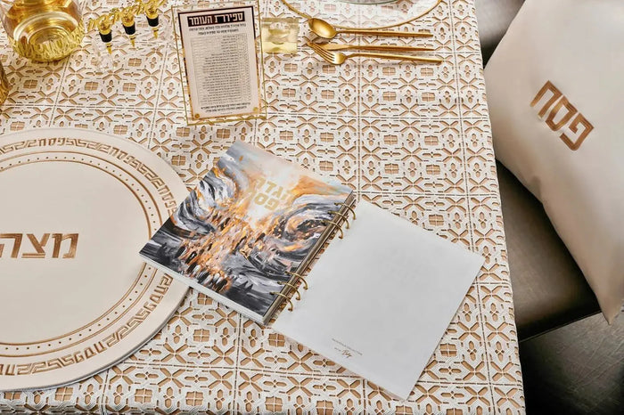 Painted by Batya lucite Haggadah displayed with gold accents, place setting, and holiday table decor for Pesach