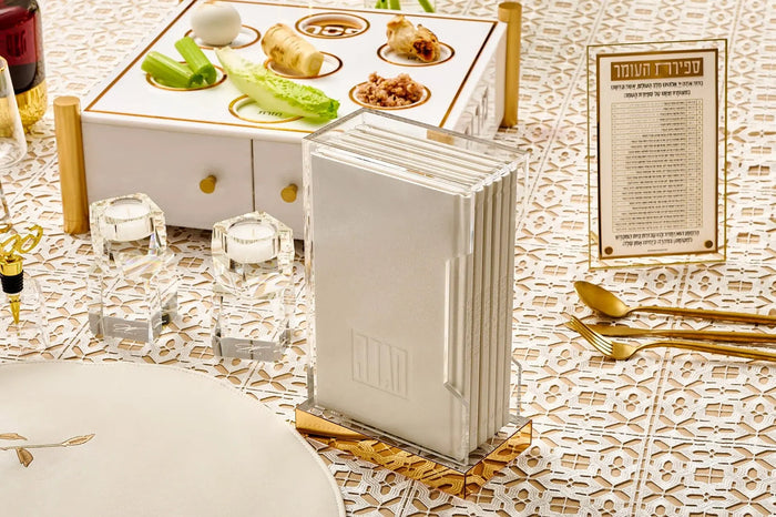 Painted hardcover Haggadah set in white and gold with matching lucite holders displayed on a decorative table setting for Passover.