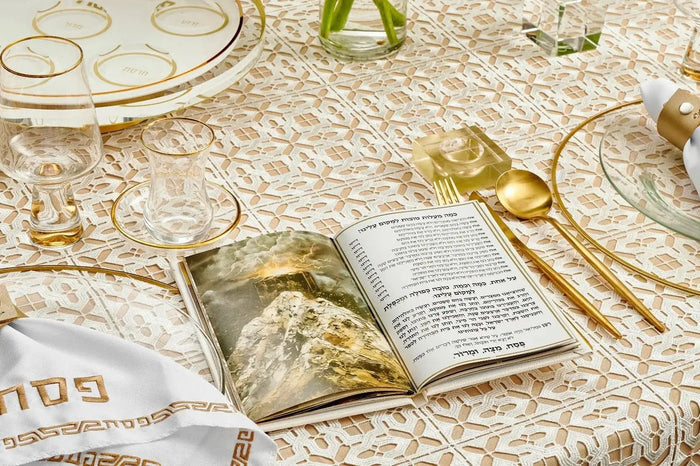 Painted Hardcover Leather & Lucite Haggadah Set displayed on elegant table with gold-rimmed glasses, utensils, and Passover place settings in white and gold tones.