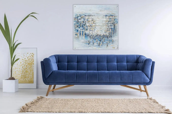 Blue modern sofa with Painted Kosel by Yosefa Jerusalem art hanging above, displayed in minimalist living room setting.