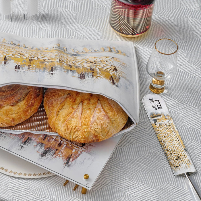 Painted Kosel knife blade cover in tan leather displayed next to challah bread and wooden board for Shabbat.