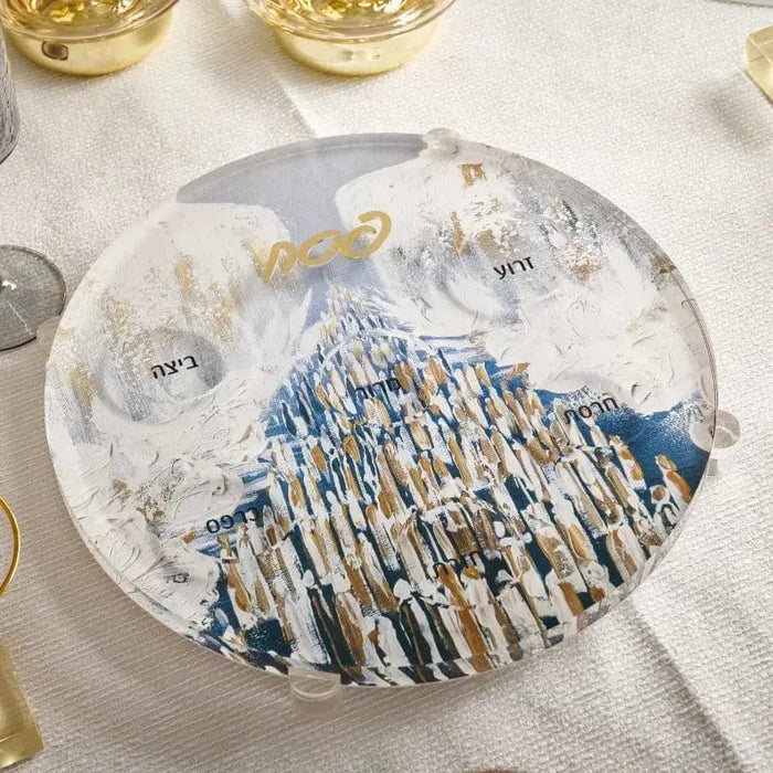 Waterdale Collection painted Seder plate with blue and white mountain landscape design on clear lucite, displayed on white table with wine glasses.