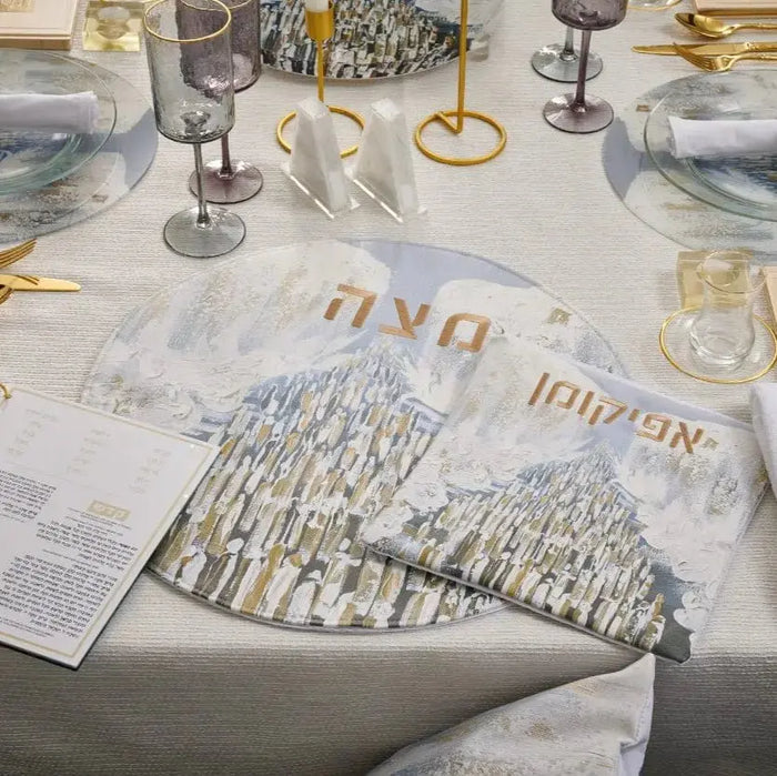 Painted Seder Plate with cityscape design in white and gold, displayed on elegant table setting with wine glasses and place settings for Pesach holiday dinner.