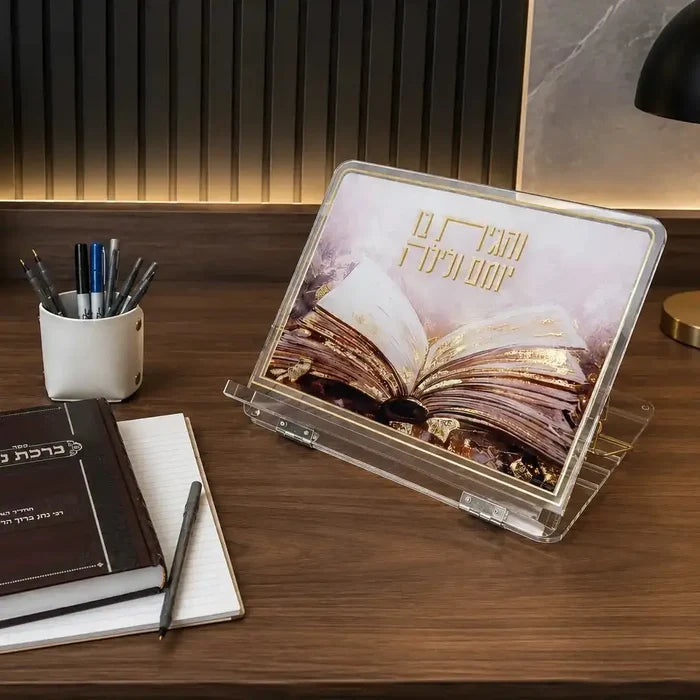 Painted Sefer foldable shtender displayed on wooden desk holding open book, with pen holder and notebooks nearby in modern study setup