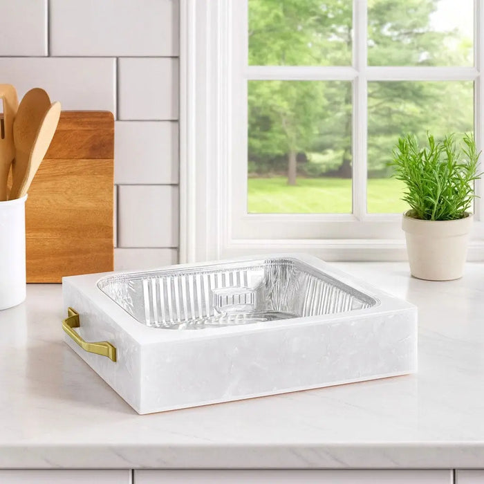 White pearl marble 9x13 pan holder by Waterdale Collection displayed on kitchen counter with cutting boards and plants nearby.