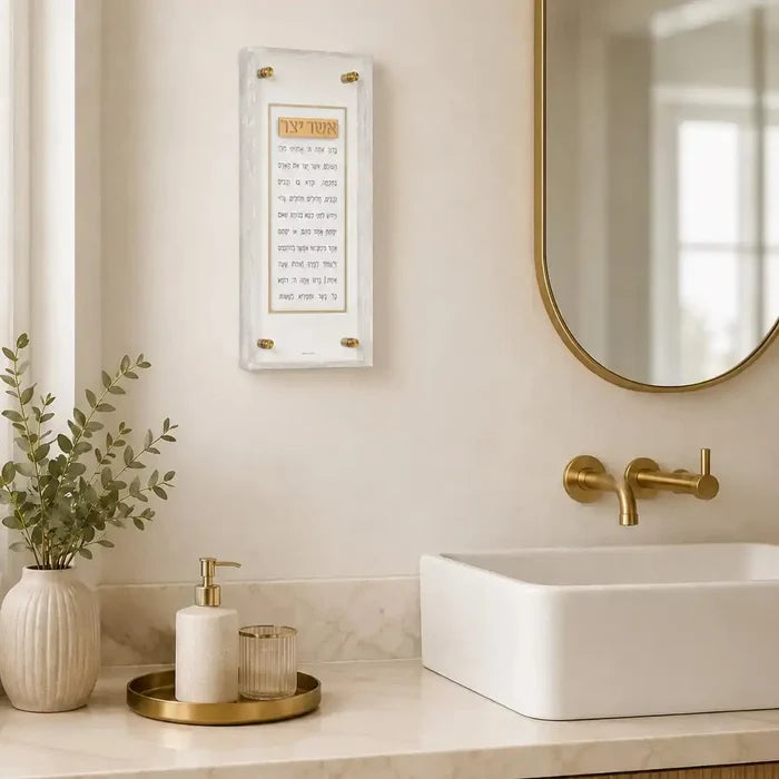 Pearlstone Frame Asher Yatzar wall art displayed above a white bathroom sink with brass fixtures and marble countertop.