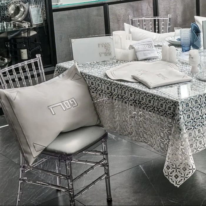 Pearlstone Pesach leather set displayed on patterned tablecloth with white pillows, plates, and place cards arranged on dining table with chrome chairs.