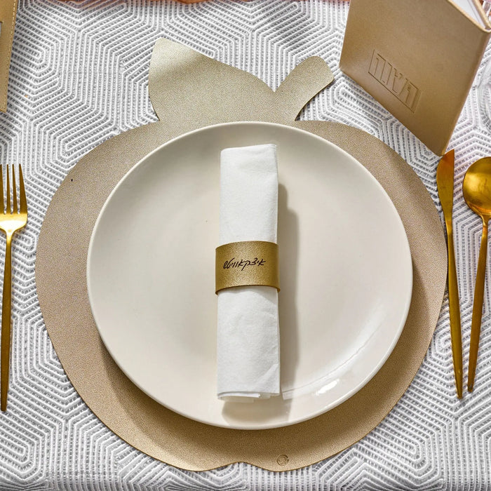 Gold leather napkin wrap holding a rolled white napkin on a place setting with gold charger plate and cutlery.