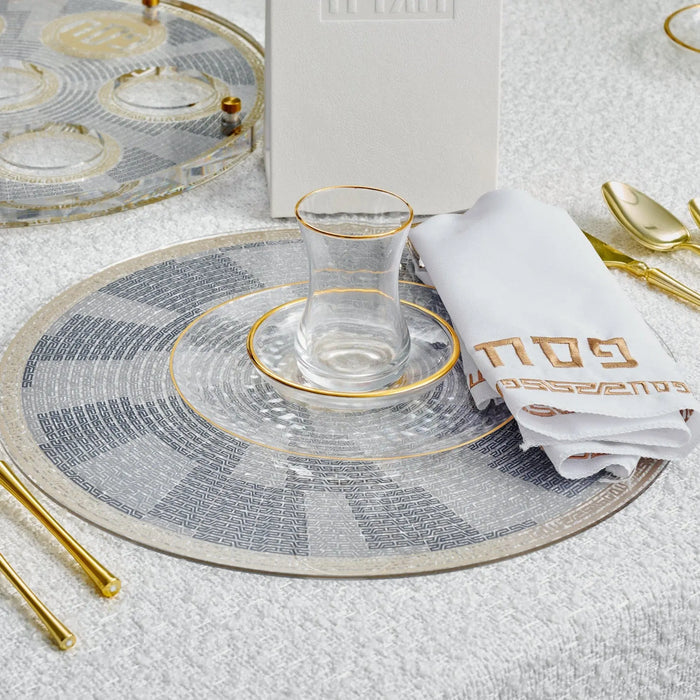 Pesach geometric charger plate in gray and gold with circular pattern design, styled on white table setting with gold cutlery and napkin.