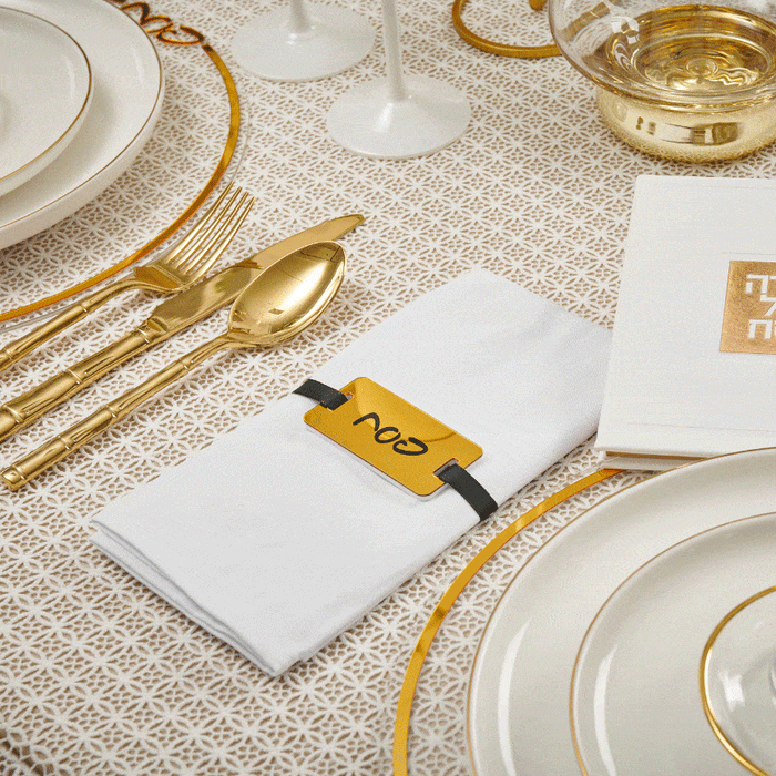 Gold Pesach napkin wraps arranged on a formal place setting with white plates and gold cutlery for holiday tabletop décor.