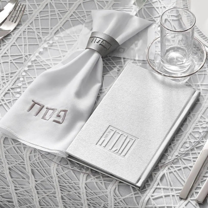 Gray Pesach napkin with napkin ring on white plate, displayed on table setting with Passover tableware and map background