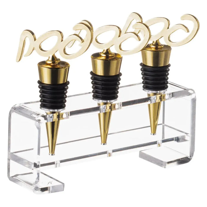 Three gold Pesach wine stoppers with decorative handles displayed in a clear acrylic stand, perfect for holiday entertaining.