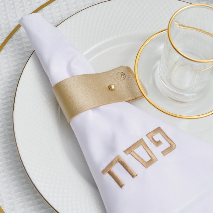 Gold leather pin napkin wraps displayed on a white plate with matching gold charger ring and white napkin for formal table setting.