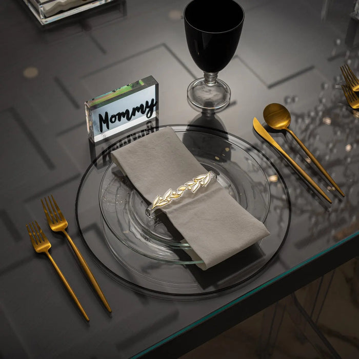 Gold pomegranate leaf napkin ring displayed on white napkin with wine glass and gold cutlery on dark table setting.