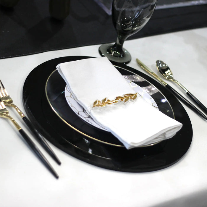 Gold pomegranate leaf napkin rings displayed on a formal place setting with black plate and white napkin, elegant tabletop styling.