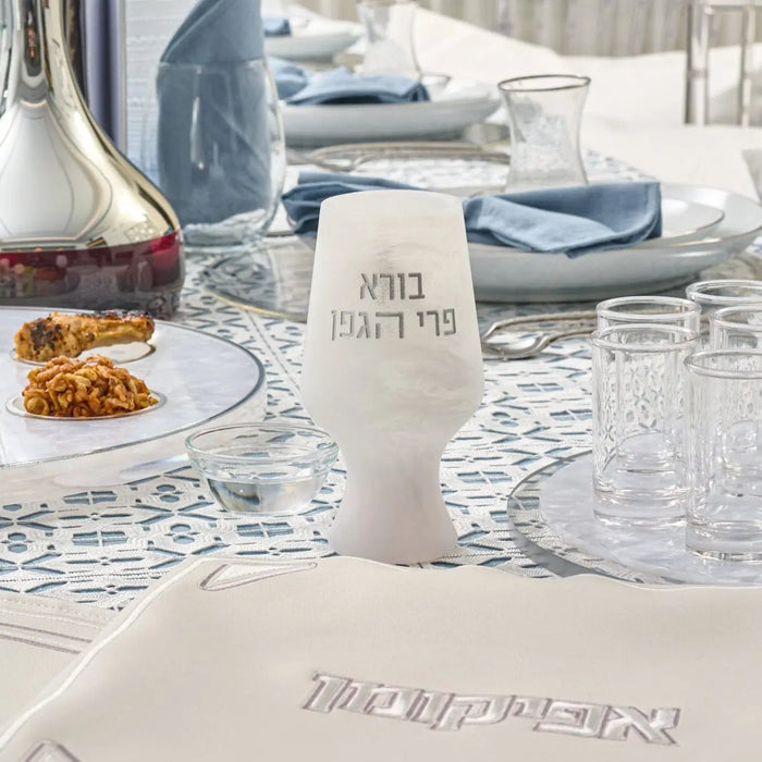 White resin Kiddush cup with Hebrew text engraving, displayed on a table setting with dishes and wine glasses for Havdalah ceremony.