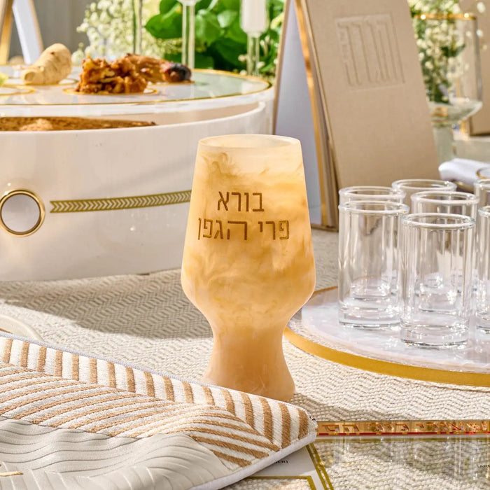 Amber resin Kiddush cup with Hebrew text, displayed on a white table setting with gold accents and glassware.