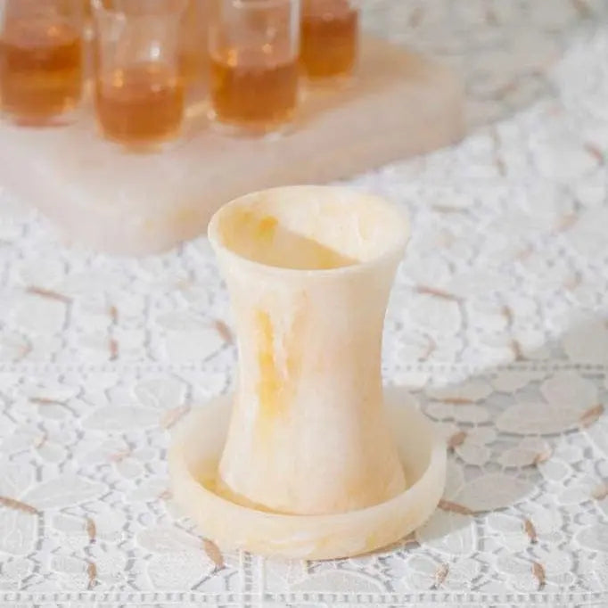 Cream-colored resin Kiddush cup with curved sides displayed on a marble surface, with additional cups visible in background.