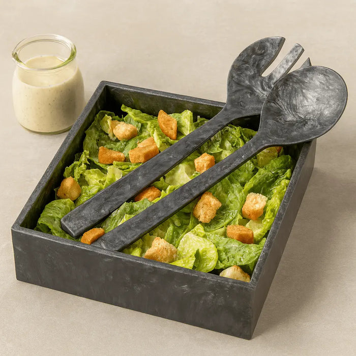 Waterdale Collection resin square salad bowl set with dark gray bowls, serving utensils, and yellow salad displayed with dressing on the side.