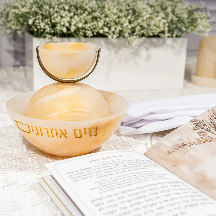 Rotating resin mayim achronim dispenser in natural wood tone on white tabletop with flowers and papers nearby