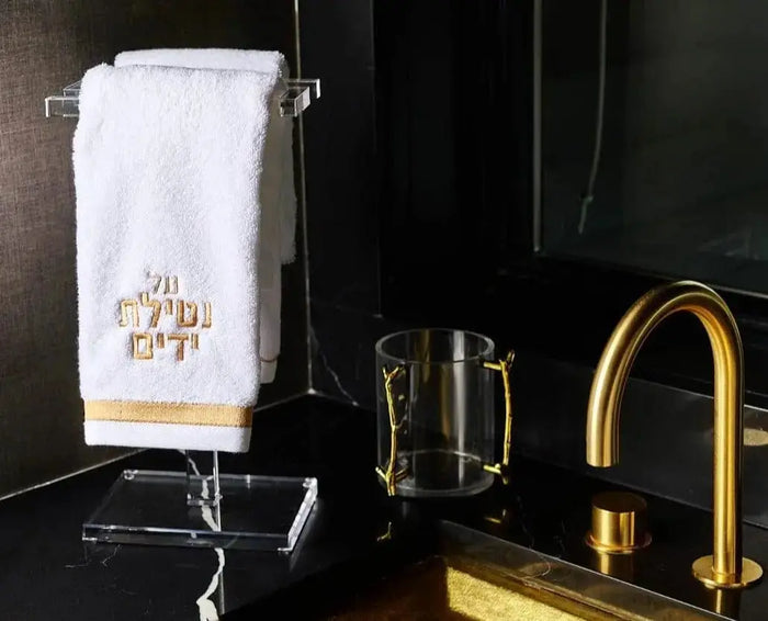 S-shaped clear acrylic finger towel stand by Waterdale Collection holding white towel on black bathroom vanity with gold faucet