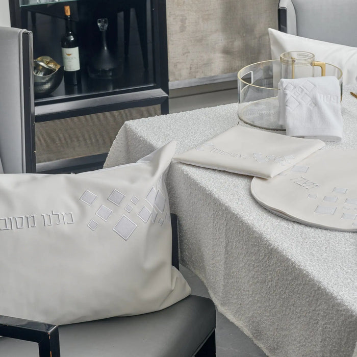 Scattered Fur Pesach Set in white leather with silver accents, displayed on a table with matching napkins and dinnerware for holiday entertaining.