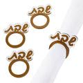 Four gold Shabbos napkin rings with Hebrew lettering displayed on white napkin, elegant tabletop décor for Shabbat meals.