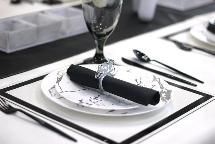 Elegant silver Shabbos napkin ring holding a black napkin on a formal place setting with white plate and silverware.