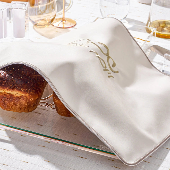 Silver leather Challah cover with gold accents displayed on a white table with bread and wine, perfect for Shabbat.