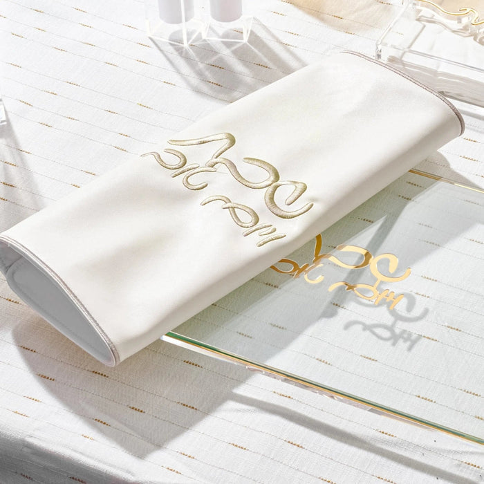 Silver classic challah cover with gold decorative handles resting on white linens and tableware for Shabbat meals.