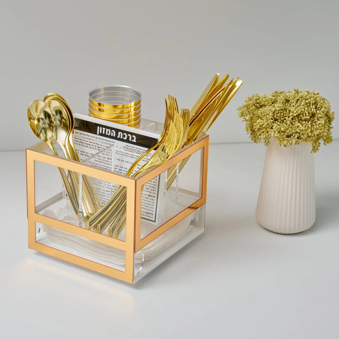 Gold silverware caddy with glass compartments holding utensils, matching white ceramic holder with dried florals, elegant table setting accessory.