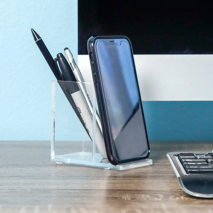 Clear acrylic pen and phone holder displaying a blue smartphone and black pens on a wooden desk.