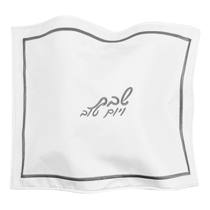 White leather challah cover with silver trim and embroidered Hebrew text, hotel-style design for Shabbat dining.