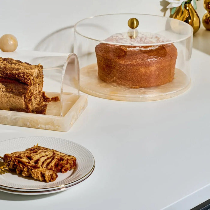 Small rectangular resin cake dome with clear acrylic cover, displayed with baked goods and gold accents on white surface.