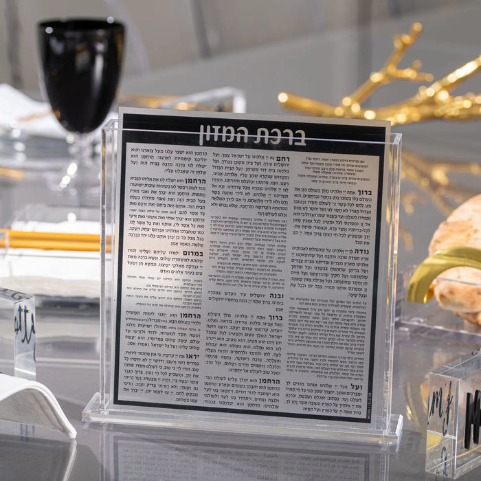 Black and silver Square Bencher Set on display table with wine glass and holiday decorations, Waterdale Collection Shabbat bencher.