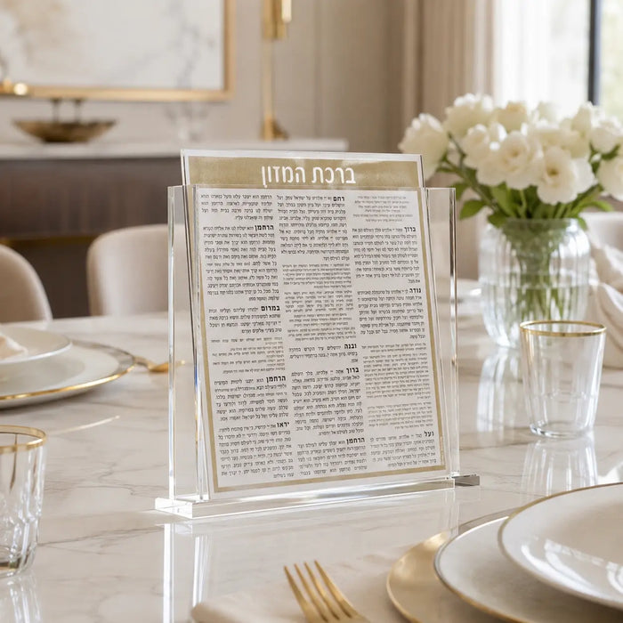 Square Bencher Set in black and gold displayed on elegant dining table with white flowers and place settings for Shabbat.